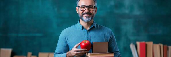Young man with glasses holding books and an apple against a teal background photo
