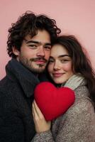 Young couple poses together with a heart shaped object against a pink backdrop photo