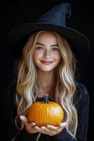 A young woman in a witch hat holds a small pumpkin, capturing the essence of autumn celebrations photo