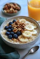 Healthy breakfast bowl with oatmeal, banana, blueberries, and walnuts beside a fresh orange juice photo