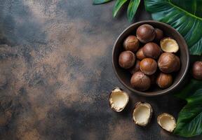 Freshly harvested nuts in a black bowl on a dark textured surface with green leaves photo