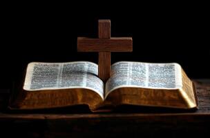 A wooden cross stands on an open Bible in a dimly lit room during evening hours photo