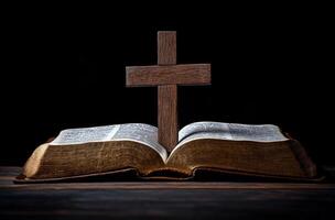 A wooden cross stands on an open Bible in a dimly lit room during evening hours photo