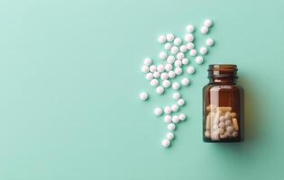 Various white pills spilled next to a glass bottle on a turquoise background at home photo