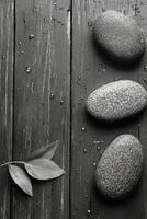 Three smooth stones and fresh leaves on a wooden surface with water droplets photo