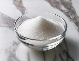 Granulated sugar in a glass bowl on a marble background photo