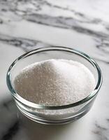 Granulated sugar in a glass bowl on a marble background photo