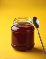 Jam jar with spoon next to it on yellow background photo
