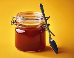 Jam jar with spoon next to it on yellow background photo
