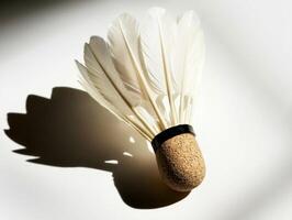 badminton shuttlecock rests on a white surface highlighting its feathered design and cork base. The bright lighting creates soft shadows enhancing its minimalist beauty. photo