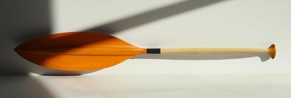 canoe paddle rests on a white background highlighting its vibrant blade shape and comfortable handle grip. Soft shadows create a striking visual effect in bright lighting. photo
