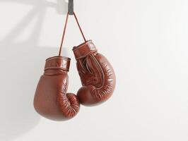 striking display features a pair of beautifully stitched red boxing gloves hanging from a hook against a plain white background illuminated by bright studio lights. photo