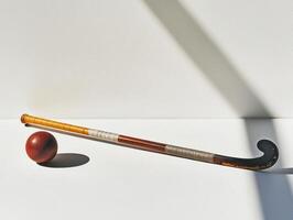 field hockey stick lies alongside a ball on a clean white surface highlighted by bright studio lighting that emphasizes the details and textures while casting soft shadows. photo