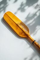 elegant design of a rowing oar resting flat against a white background. The soft midday light highlights the fine details of the blade and handle casting gentle shadows. photo