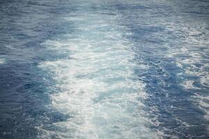 Wake of a ship creating frothy, white trails on the blue ocean surface. photo