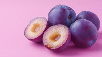 Plums stacked on pink surface with sliced one photo
