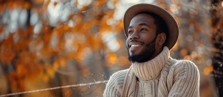 A man in a sweater and hat smiles in the fall photo