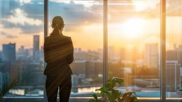 A woman in a suit stands in front of a window looking out at the city photo