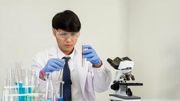 Man asian student education learning scientist wearing doctor gown in lab looking hand at chemist. caused by mixing reagents in scientific research laboratories with test tubes and microscope on table photo