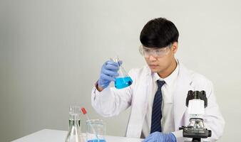 Man asian student education learning scientist wearing doctor gown in lab looking hand at chemist. caused by mixing reagents in scientific research laboratories with test tubes and microscope on table photo