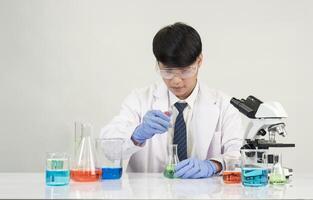 Man asian student education learning scientist wearing doctor gown in lab looking hand at chemist. caused by mixing reagents in scientific research laboratories with test tubes and microscope on table photo
