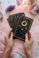 A person holding tarot cards surrounded by crystals on a pink surface with decorative elements photo