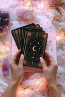 A person holding tarot cards surrounded by crystals on a pink surface with decorative elements photo