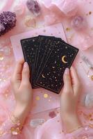 A person holding tarot cards surrounded by crystals on a pink surface with decorative elements photo