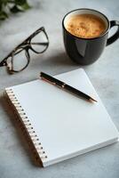 Blank notebook, pen, glasses, and coffee cup arranged on a gray desk for creative brainstorming photo