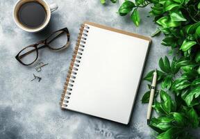 Coffee cup, notebook, and glasses on a textured surface amidst greenery in a cozy workspace photo