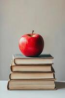 A vibrant red apple resting atop three stacked books on a sunny surface with shadows photo
