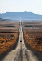 A winding road stretches through an arid desert landscape with distant mountains on a sunny day photo