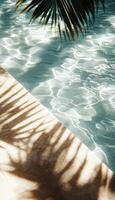 Tranquil sunlight reflecting on clear pool water beside a serene stone patio with palm leaves photo