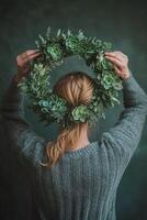 Young woman wearing a cozy sweater holds a lush green wreath adorned with succulents indoors photo