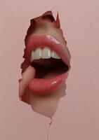 A close up view of a mouth breaking through pink paper with glossy lips and white teeth photo