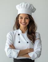 Smiling female chef wearing a white uniform and hat poses confidently in a bright kitchen photo