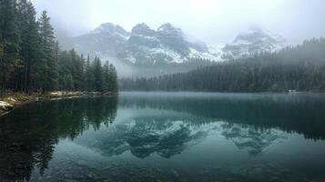 A tranquil lake surrounded by misty mountains and dense evergreen forests in early morning photo