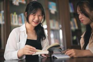 Two women are sitting at a table in a library, one of them reading a book photo