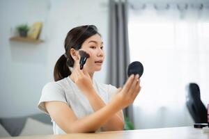 Asian woman is applying makeup in front of a mirror. She is using a brush to apply the makeup photo