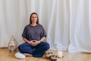 A smiling woman sits in lotus position, preparing for a yoga and breathing practice with a calm focus. photo