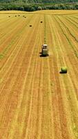 Aerial view of a tractor working on the field. Agricultural works of collecting dry grass in summer on the natural landscape. Vertical video