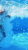 Boy jumping into the clear water in the swimming pool. Young guy jumps underwater on a blue background. Water with bubbles inside the pool. Vertical video