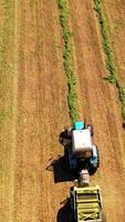 Drone view of agricultural machine working on the field. Tractor collects dried grass for feeding livestock. Motion camera bottom up. Vertical video