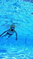 Underwater camera shoots a of a boy inside the pool. Little boy diving with mask underwater in swimming pool. Vertical video