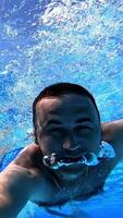 Swimmer swims forward while looking at camera underwater. Man swimming in clear water with underwater camera inside the swimming pool. Summer vacation. Vertical video