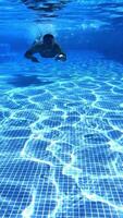 Man swimming under water in the pool. Underwater view of a male swimmer floating in transparent water to the camera. Vertical video
