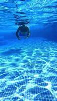Man underwater. Blue transparent water inside the swimming pool and a swimmer male swimming and looking under water to camera. Vertical video