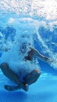 Man jumps into clear water of a pool in yoga pose. Underwater camera shooting a of a man jumping into water. Male shows gesture yes with thumbs underwater. Vertical video