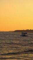 Catamaran and people in the evening sea. Blue boat floating on the background of the calm sea at sunset. People swimming in water. Vertical video