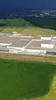 Aerial view from afar on manufacturing complex. Large industrial territory surrounded by green fields and forests in summer. Camera moves down. Vertical video